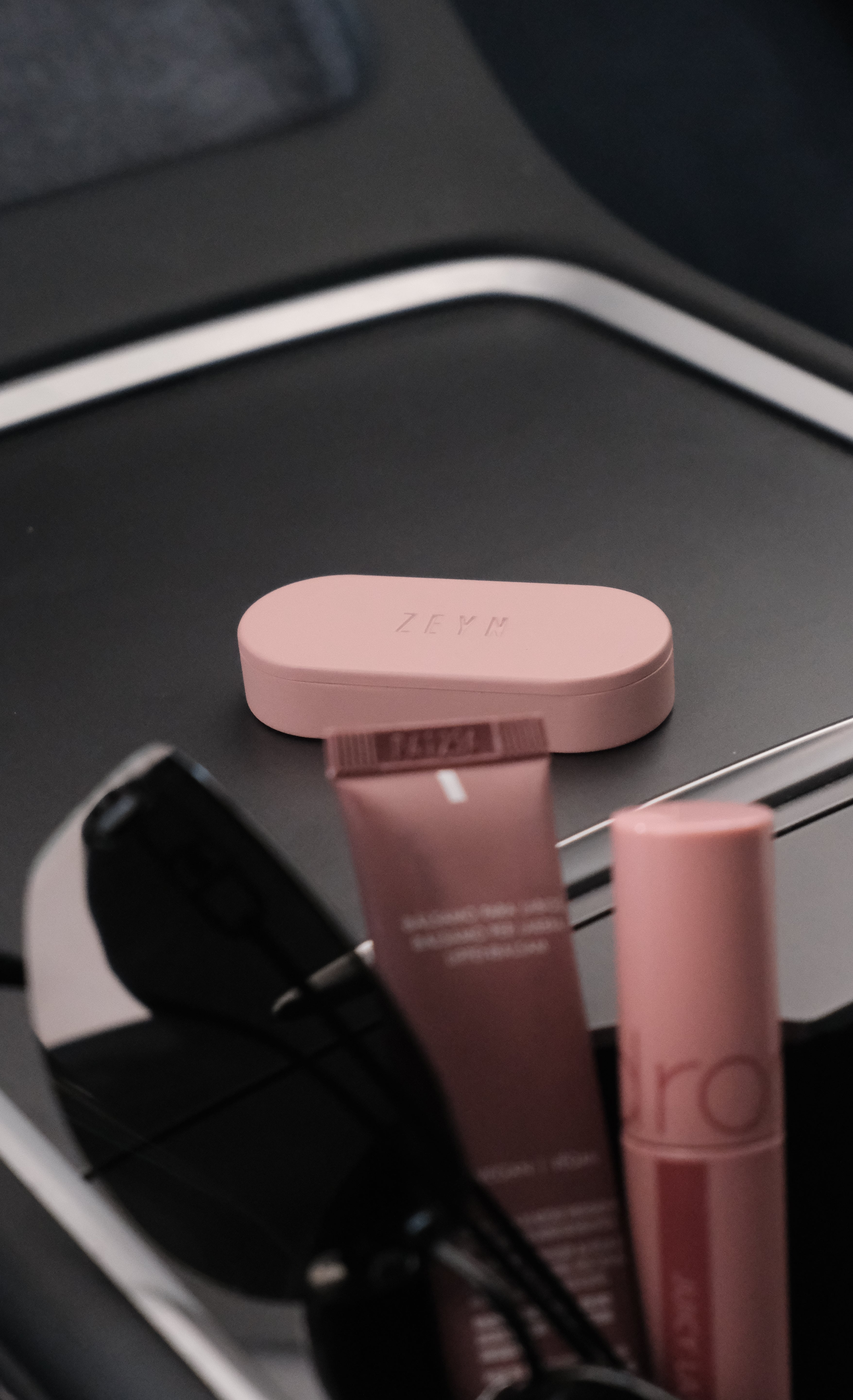Two pink lip products on a car dashboard with Zeyn solid perfume balm device 