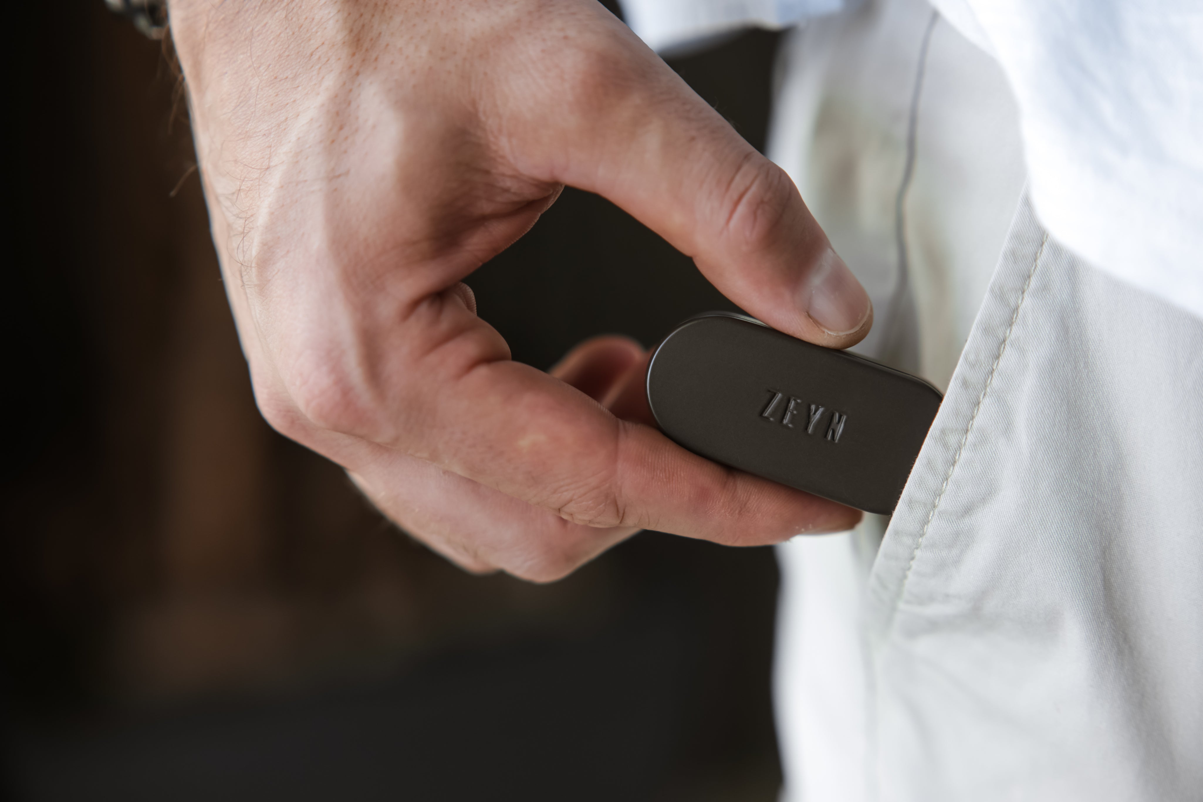 Hand holding a black device labeled 'ZEYN' against a blurred background
