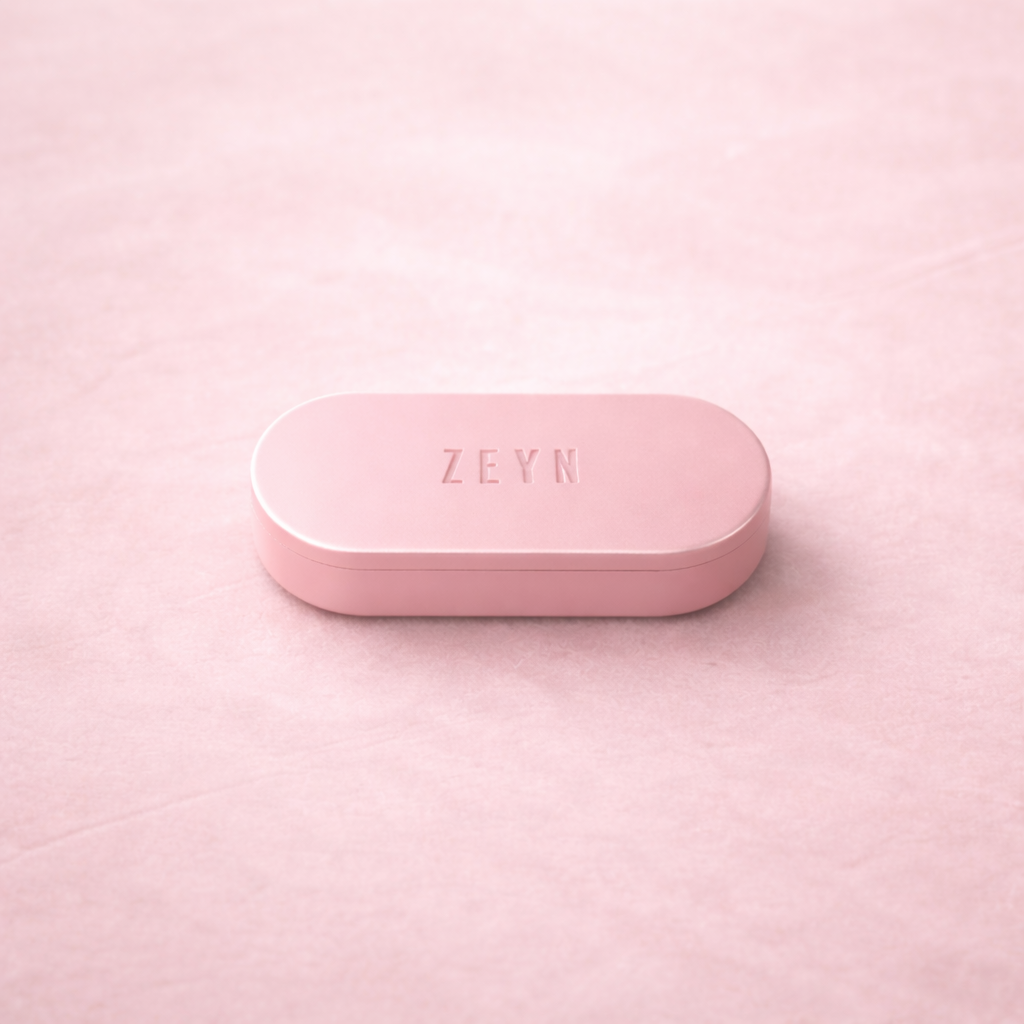 Soft pink ZEYN refillable perfume balm device closed on a textured pink background.