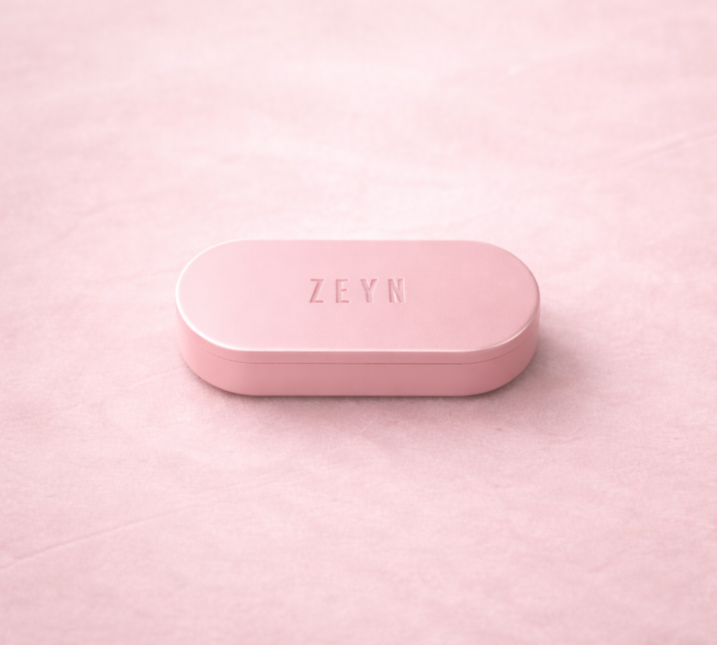 Soft pink ZEYN refillable perfume balm device closed on a textured pink background.